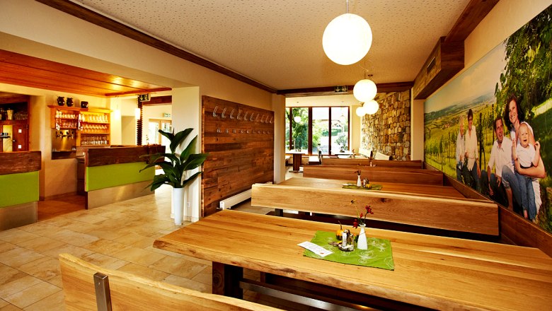 Winzerhaus Kattner, © Winzerhaus Kattner Innenansicht eines gemütlichen Restaurants mit Holztischen und -bänken, dekoriert mit Pflanzen und einem großen Wandbild.