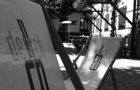 Liegestühle, © Dersch Schwarz-weiß Foto von Liegestühlen im Freien vor einem Gebäude.