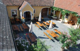 Buschenschank Hauck, © Familie Hauck Innenhof einer Buschenschank mit Holztischen und Sonnenschirmen.