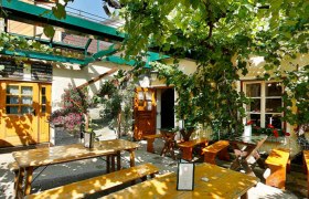 Innenhof, © Leeb Johannes Ein gemütlicher Innenhof mit Holzbänken und Tischen, umgeben von grünen Weinreben und Pflanzen.