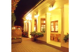 Heuriger Gilg, © Weingut Gilg Beleuchteter Eingangsbereich eines traditionellen Gebäudes mit Säulen und Blumen.