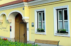 Aussenansicht, © Weingut Drimmel Urbanuskeller Gelbes Gebäude mit weißen Fensterrahmen und Holztür.