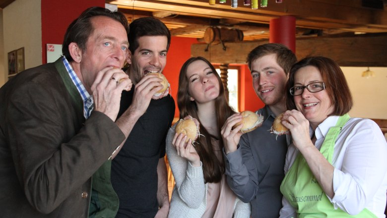 Familie Nastl, © Familie Nastl Fünf Personen essen gemeinsam belegte Brötchen in einem gemütlichen Raum.