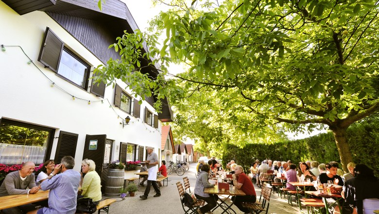 Heurigenbetrieb Nadler, © Nadler Menschen sitzen an Tischen im Freien unter Bäumen bei einem Heurigenbetrieb.