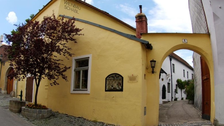 Eingangsbereich, © Mattias Reisenhofer Gelbes Gebäude mit der Aufschrift 'Weinbau Schabl', daneben ein Torbogen und ein Baum.