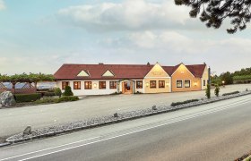 Weingut Humer - Heuriger, © Martin Sommer Außenansicht eines Weinguts mit gelbem Gebäude und rotem Dach, umgeben von Weinreben und einer Straße im Vordergrund.