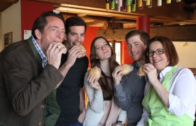 Familie Nastl, © Familie Nastl Fünf Personen essen gemeinsam belegte Brötchen in einem gemütlichen Raum.