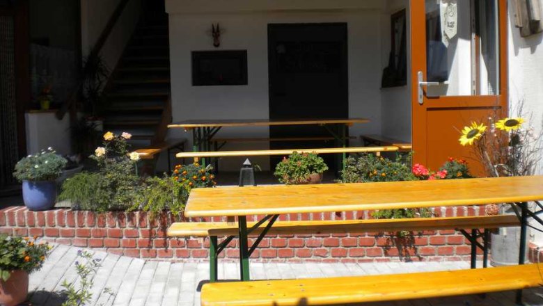 Ein gem&uuml;tlicher Au&szlig;enbereich eines Heurigen mit Holzb&auml;nken und Blumen.