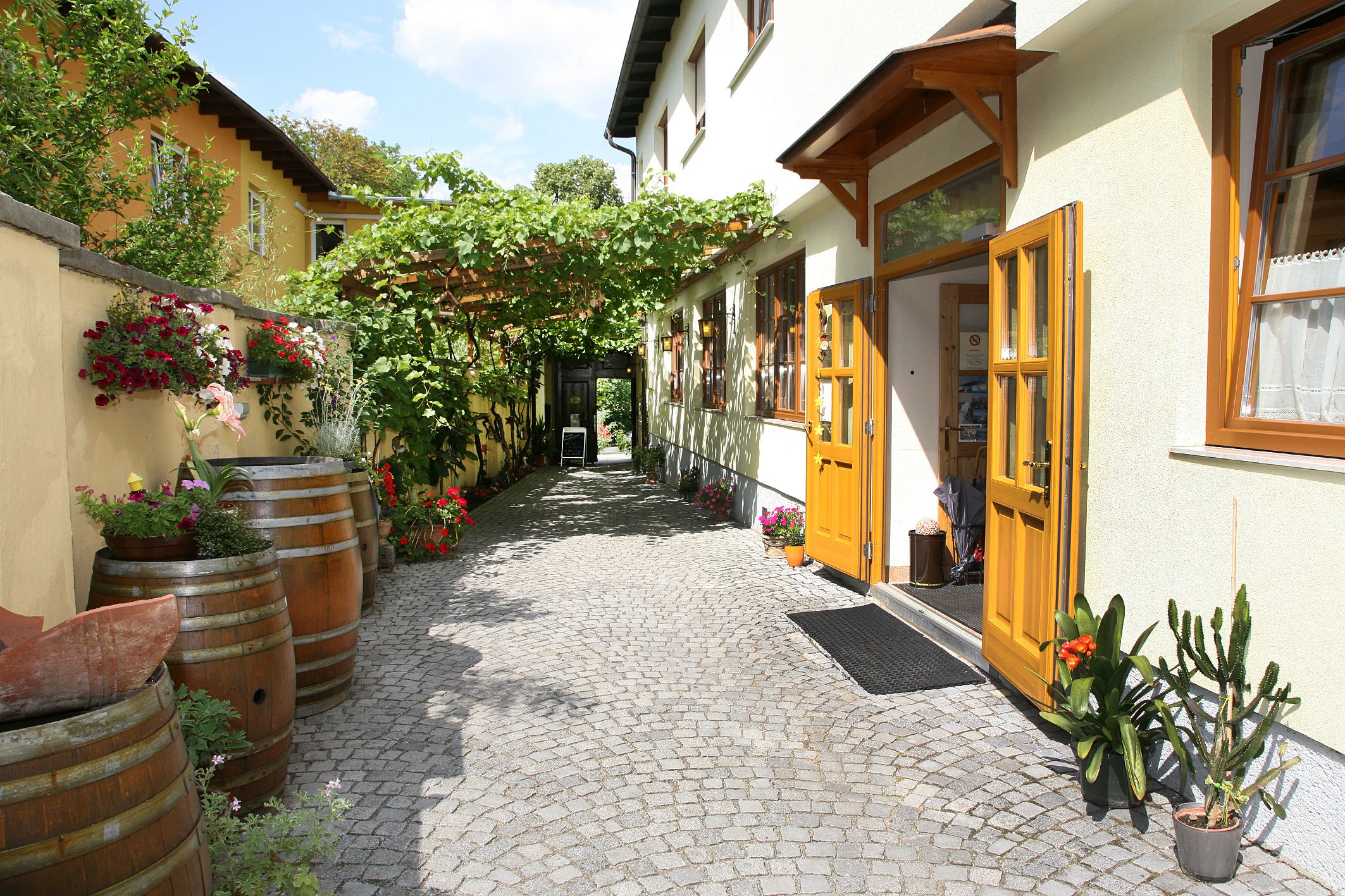 Eingang eines Heurigen mit gelben Türen, Pflastersteinen und Pflanzen.
