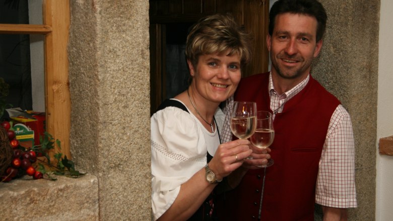 Zwei Personen in traditioneller Kleidung stoßen mit Weingläsern an.