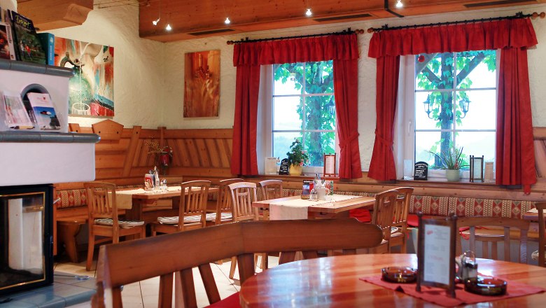 Gemütlicher Innenraum eines traditionellen österreichischen Heurigen mit Holzmöbeln und roten Vorhängen.