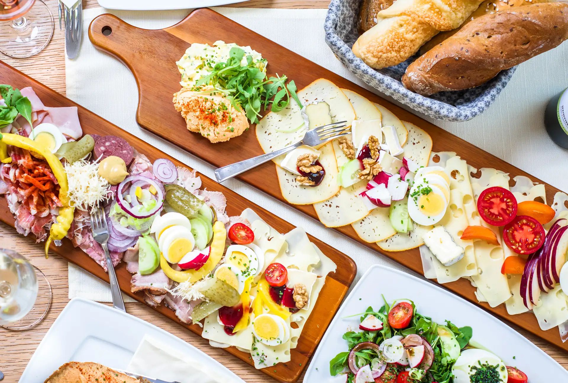 Verschiedene Aufschnitt- und Käseplatten mit Brot und Salat auf einem Tisch.