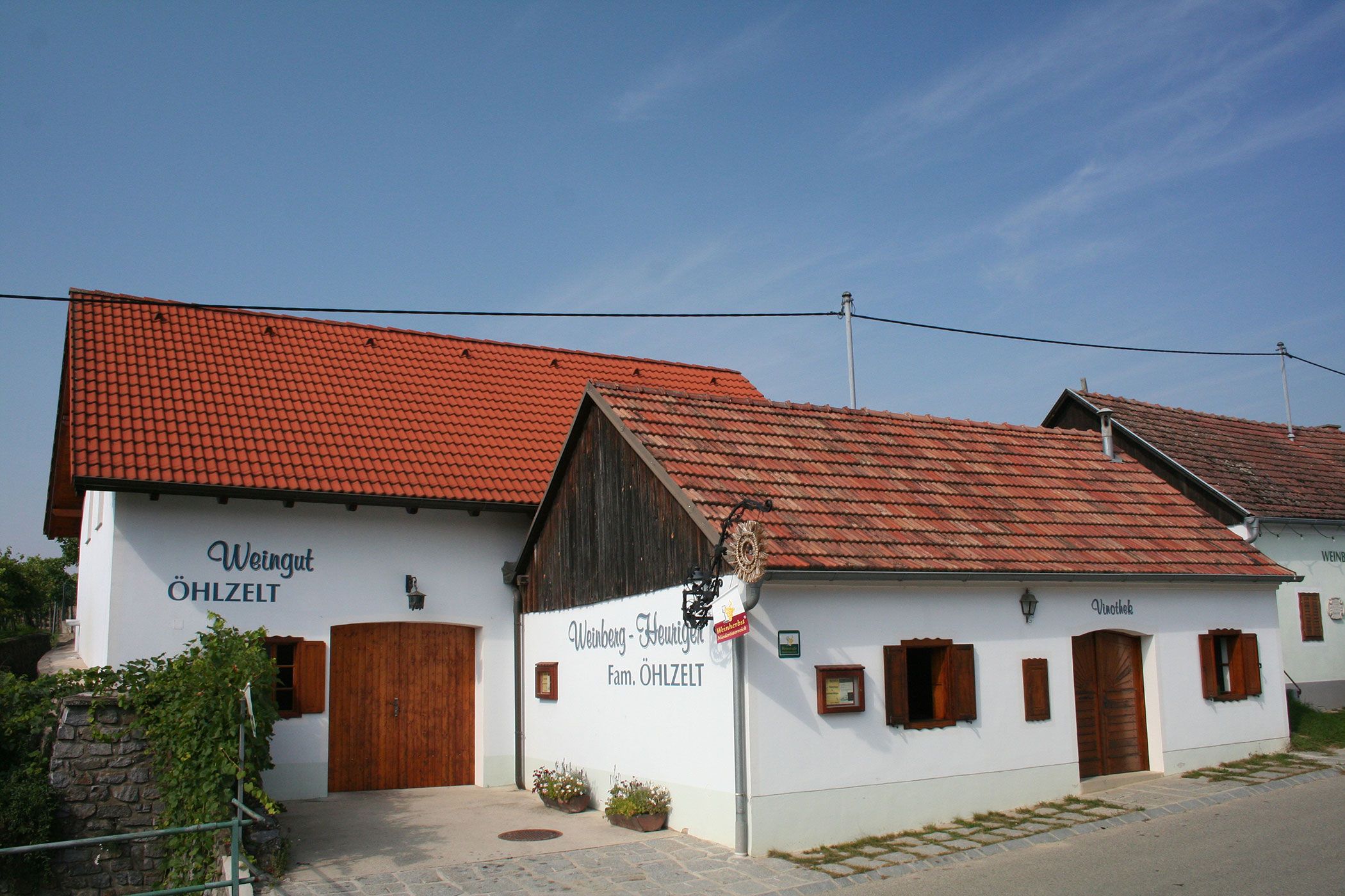 Außenansicht eines traditionellen Heurigenlokals mit weißen Wänden und roten Ziegeldächern.