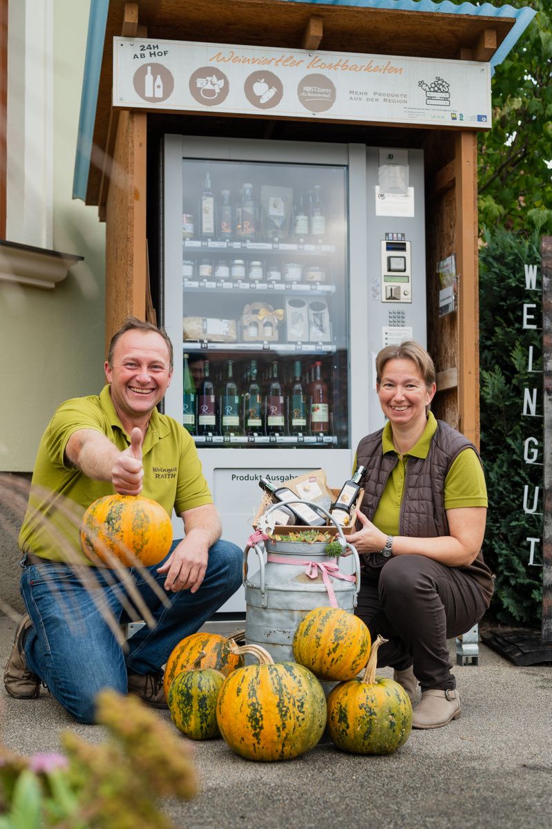 Zwei Personen vor einem Selbstbedienungsautomaten mit Kürbissen und regionalen Produkten.