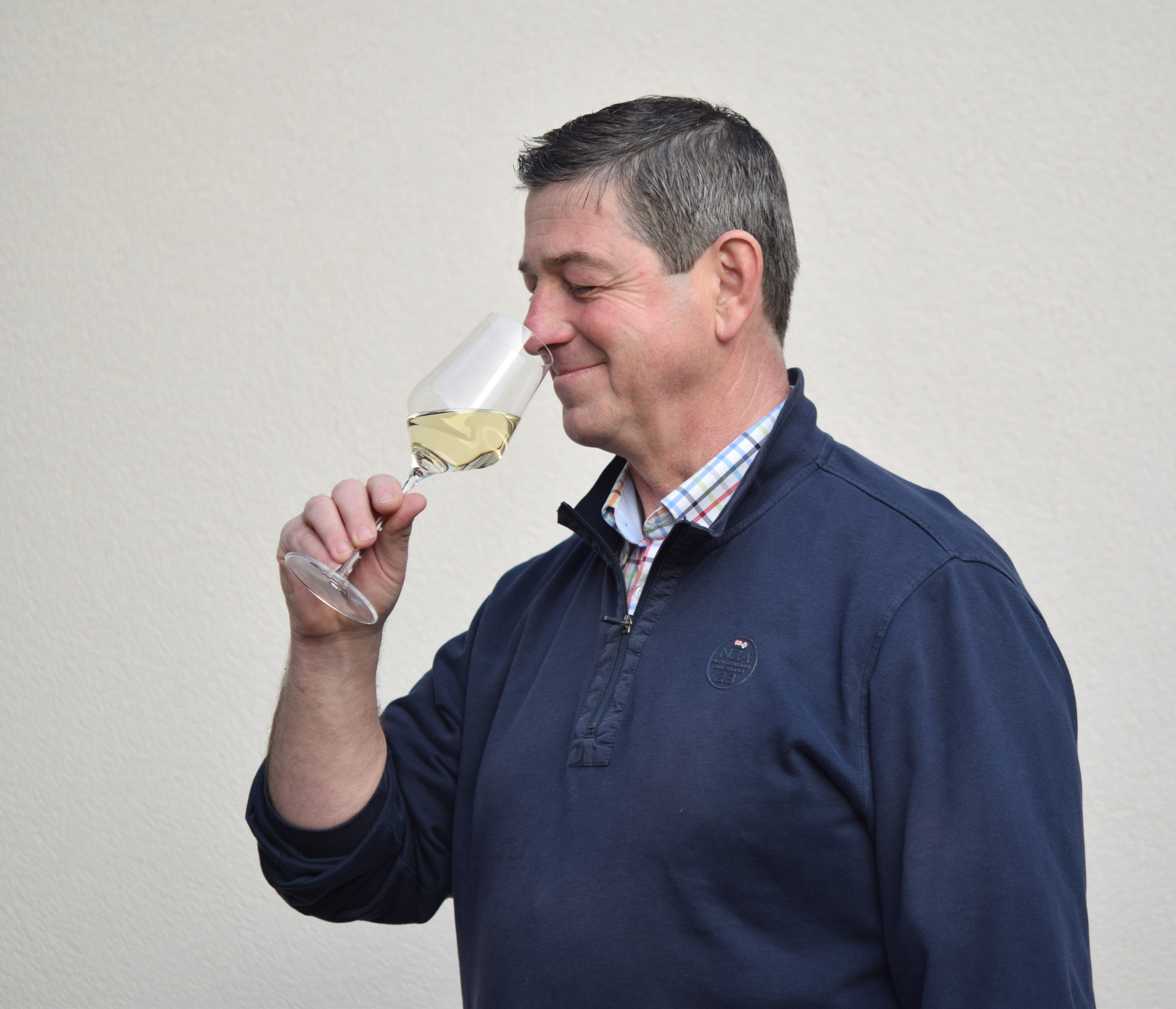 Mann riecht an einem Glas Weißwein vor neutralem Hintergrund.