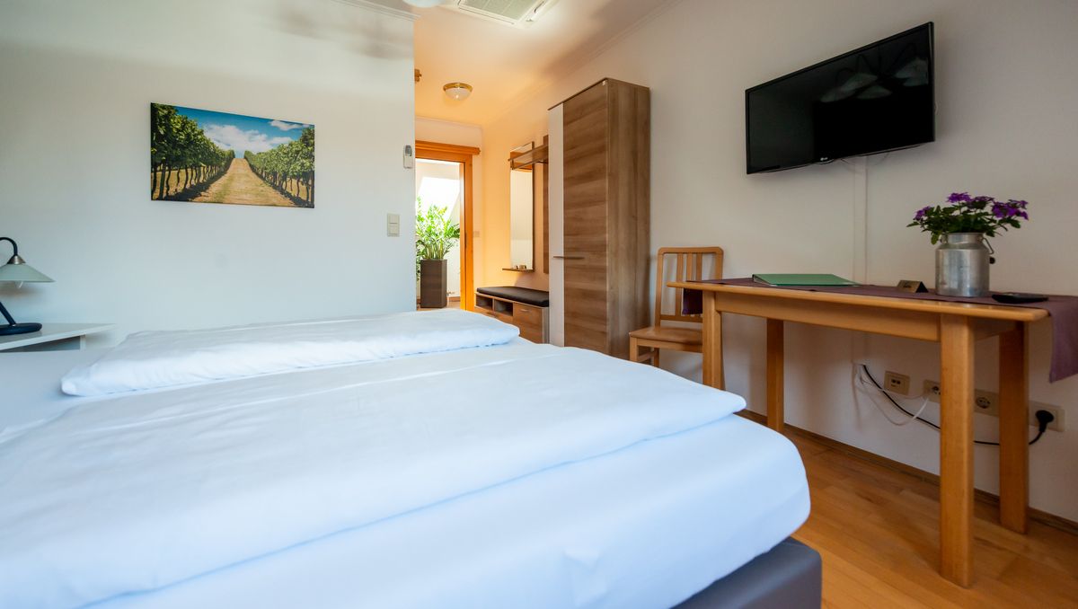 Gemütliches Hotelzimmer mit Doppelbett, Holzmöbeln, TV und Pflanzen.