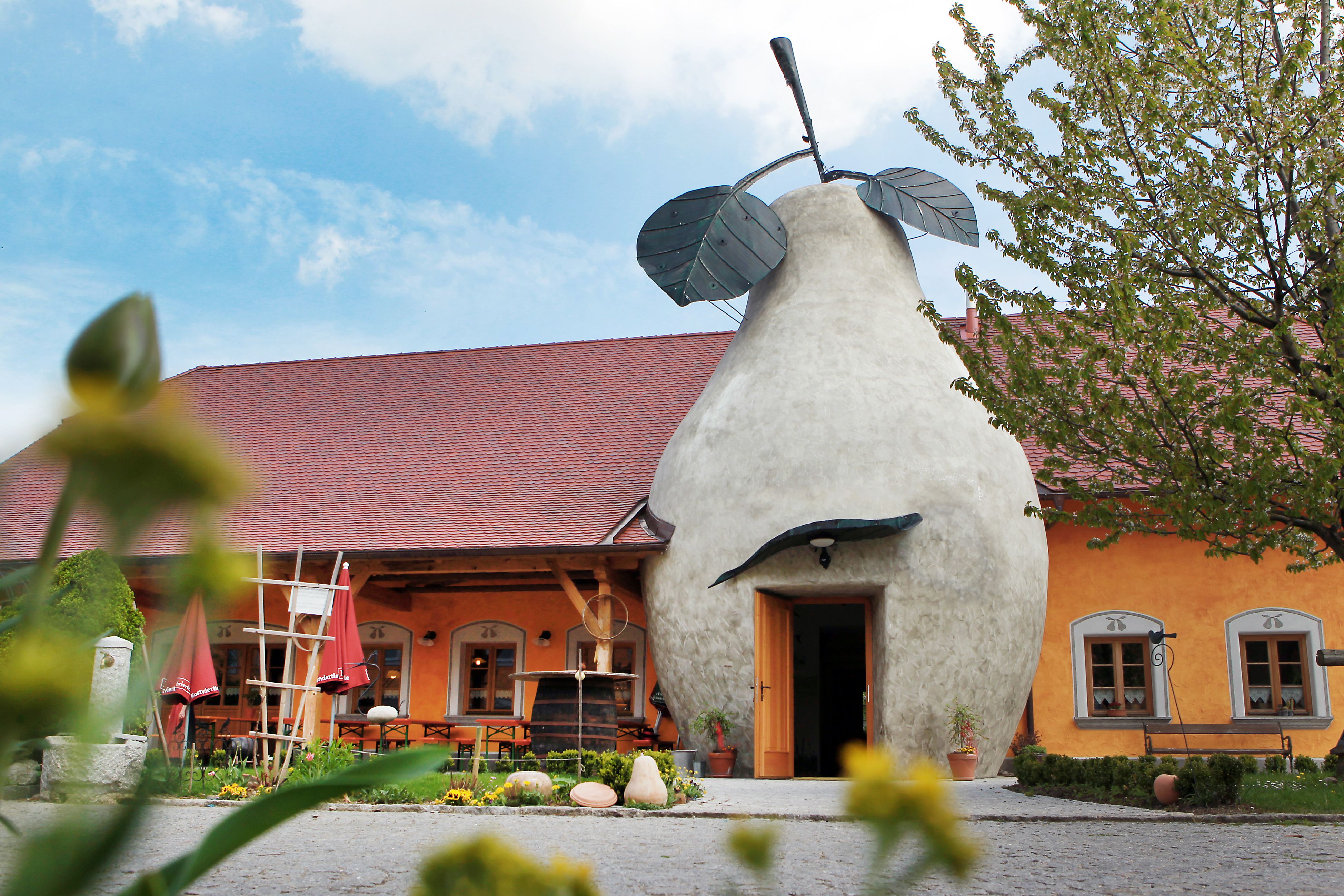 Gebäude mit birnenförmigem Eingang und rotem Dach, umgeben von Pflanzen.