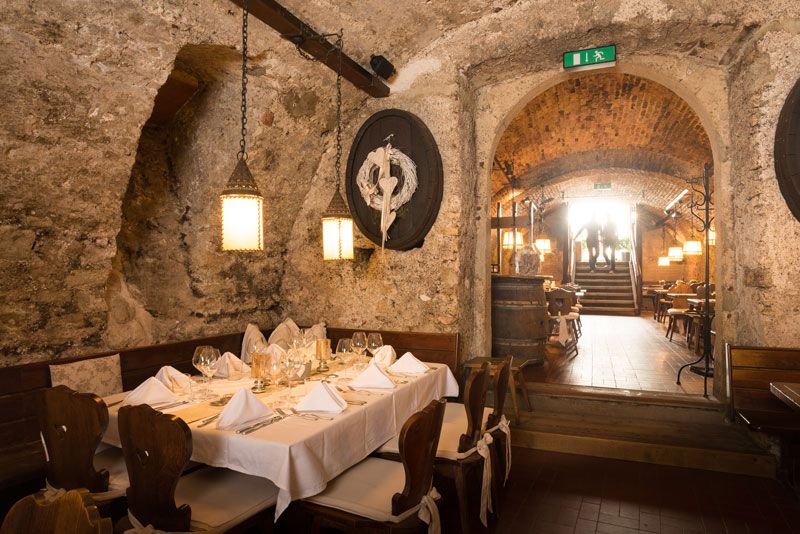 Ein rustikales Kellerrestaurant mit gedecktem Tisch, Steinwänden und Holzmöbeln.