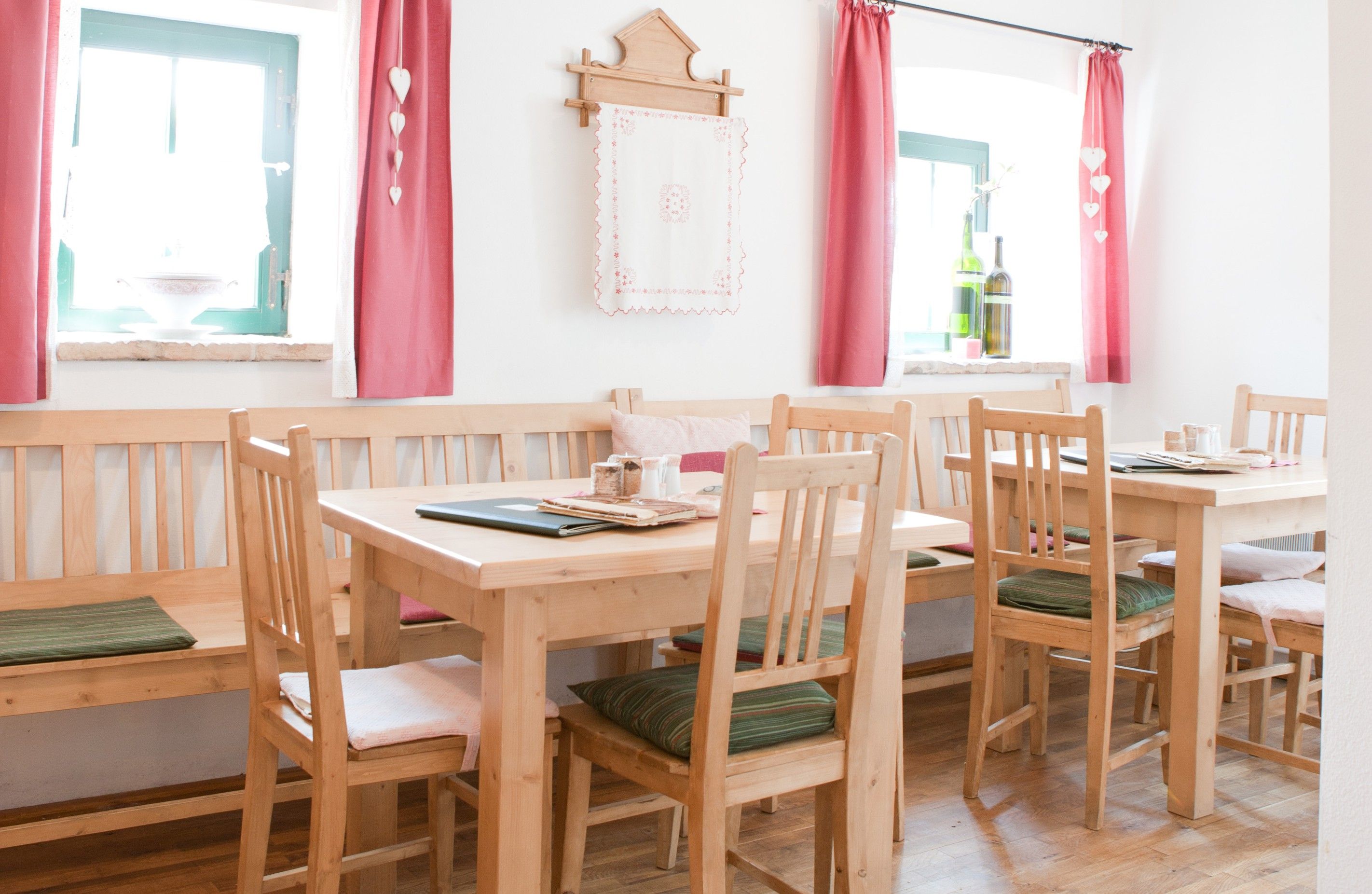 Gemütlicher Gastraum mit Holzmöbeln, roten Vorhängen und Dekoration.