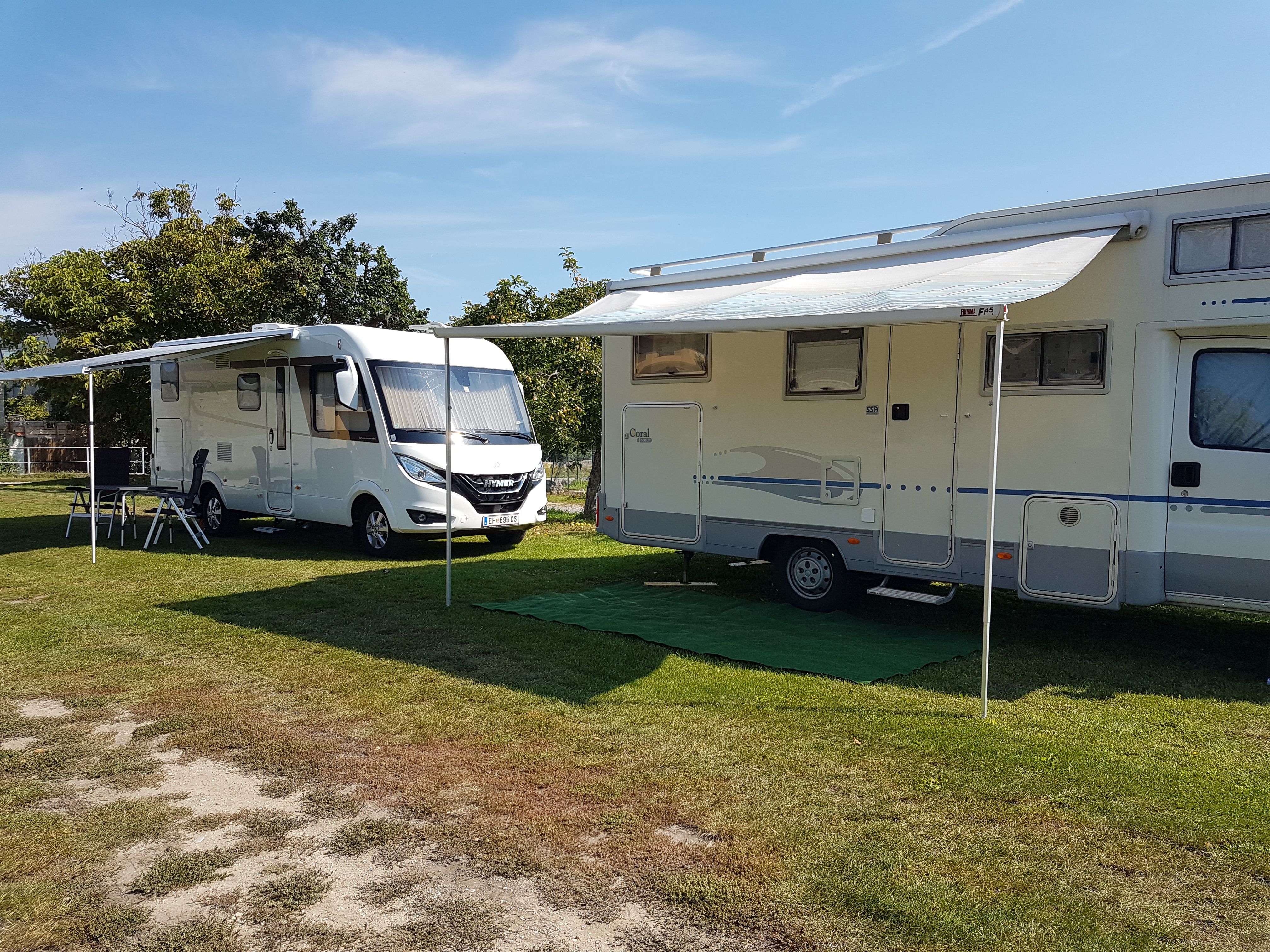 Zwei Wohnmobile mit ausgefahrenen Markisen auf einem Campingplatz.
