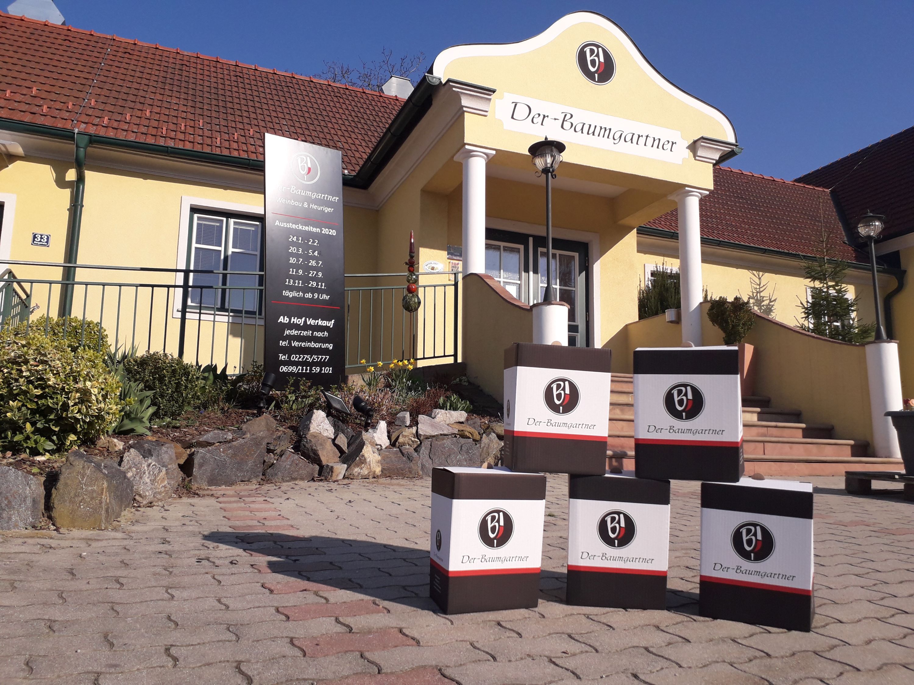 Außenansicht eines gelben Gebäudes mit der Aufschrift 'Der-Baumgartner'. Vor dem Eingang stehen Kartons mit dem Logo 'BJ'.