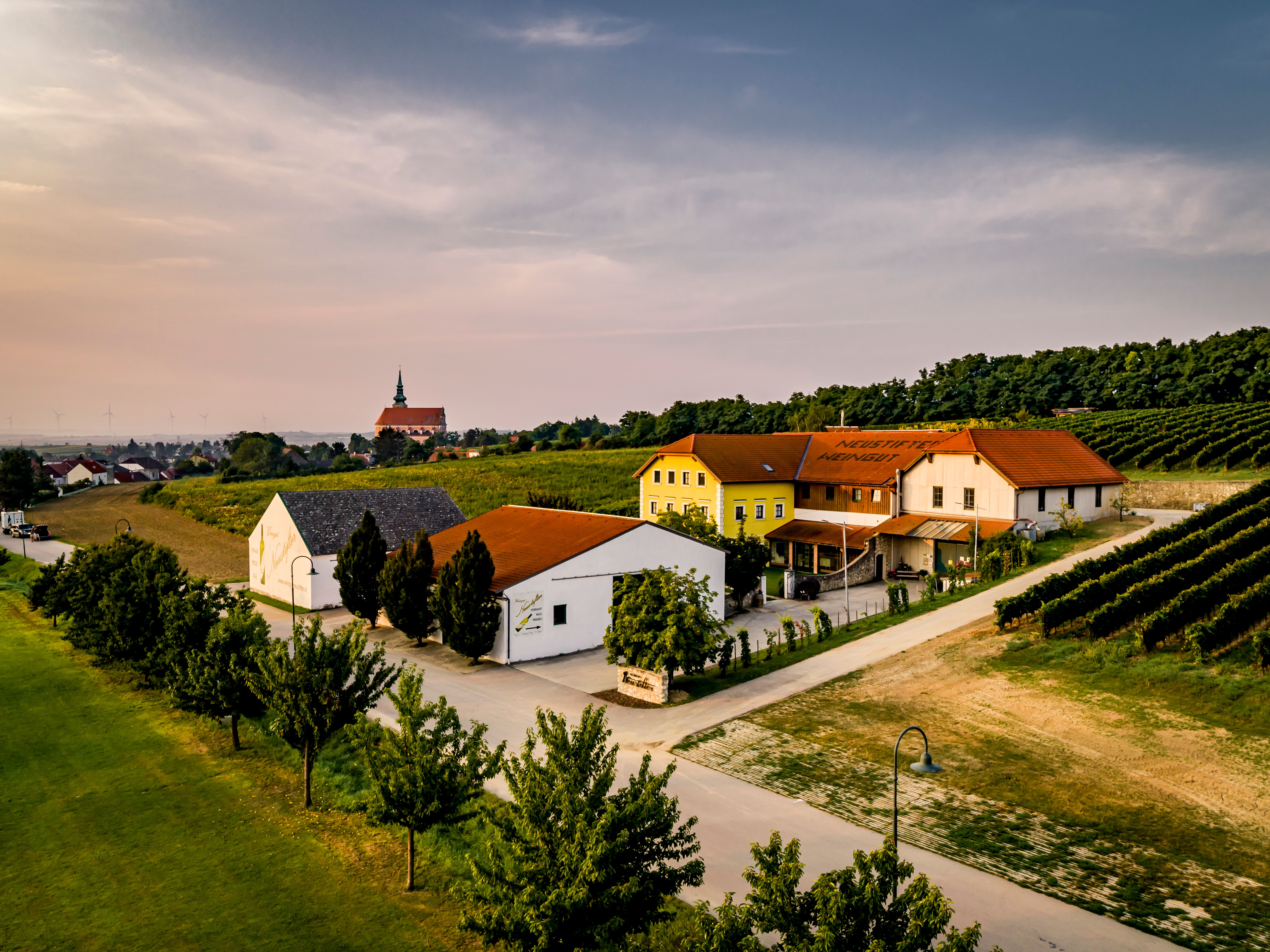 Luftaufnahme eines Weinguts mit Gebäuden und Weinbergen bei Sonnenuntergang.