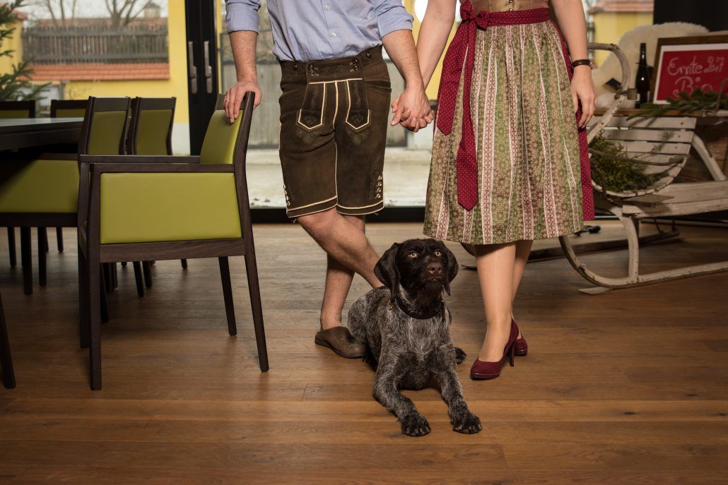 Ein Paar in traditioneller Kleidung hält Händchen, ein Hund sitzt zu ihren Füßen.