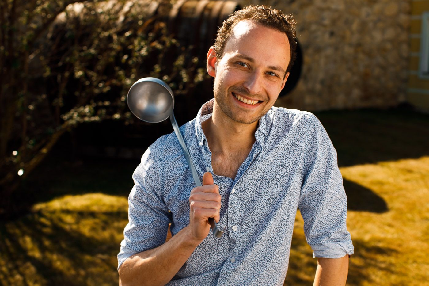 Ein lächelnder Mann im Freien hält eine große Kelle in der Hand.