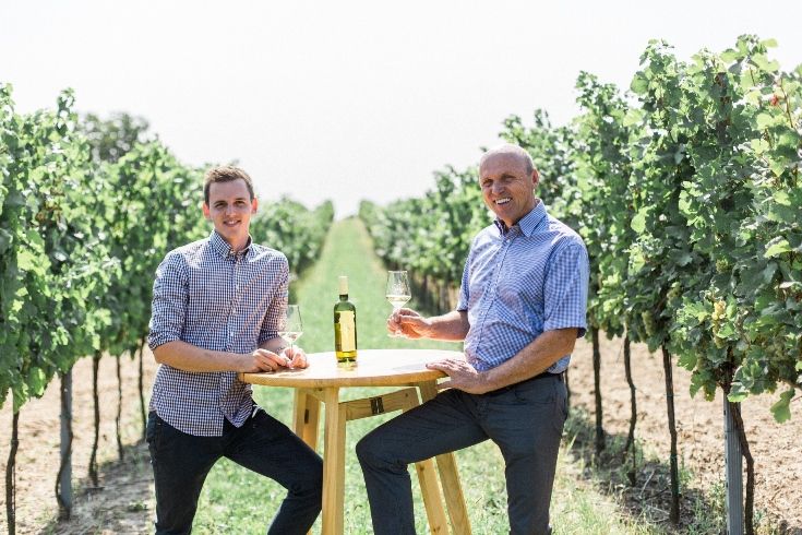 Zwei Männer sitzen an einem Tisch im Weinberg mit Weingläsern.