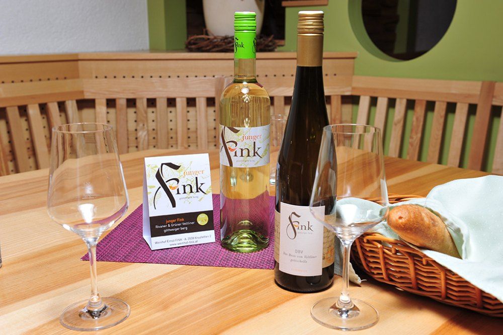 Zwei Weinflaschen und Gläser auf einem Holztisch mit Brotkorb.