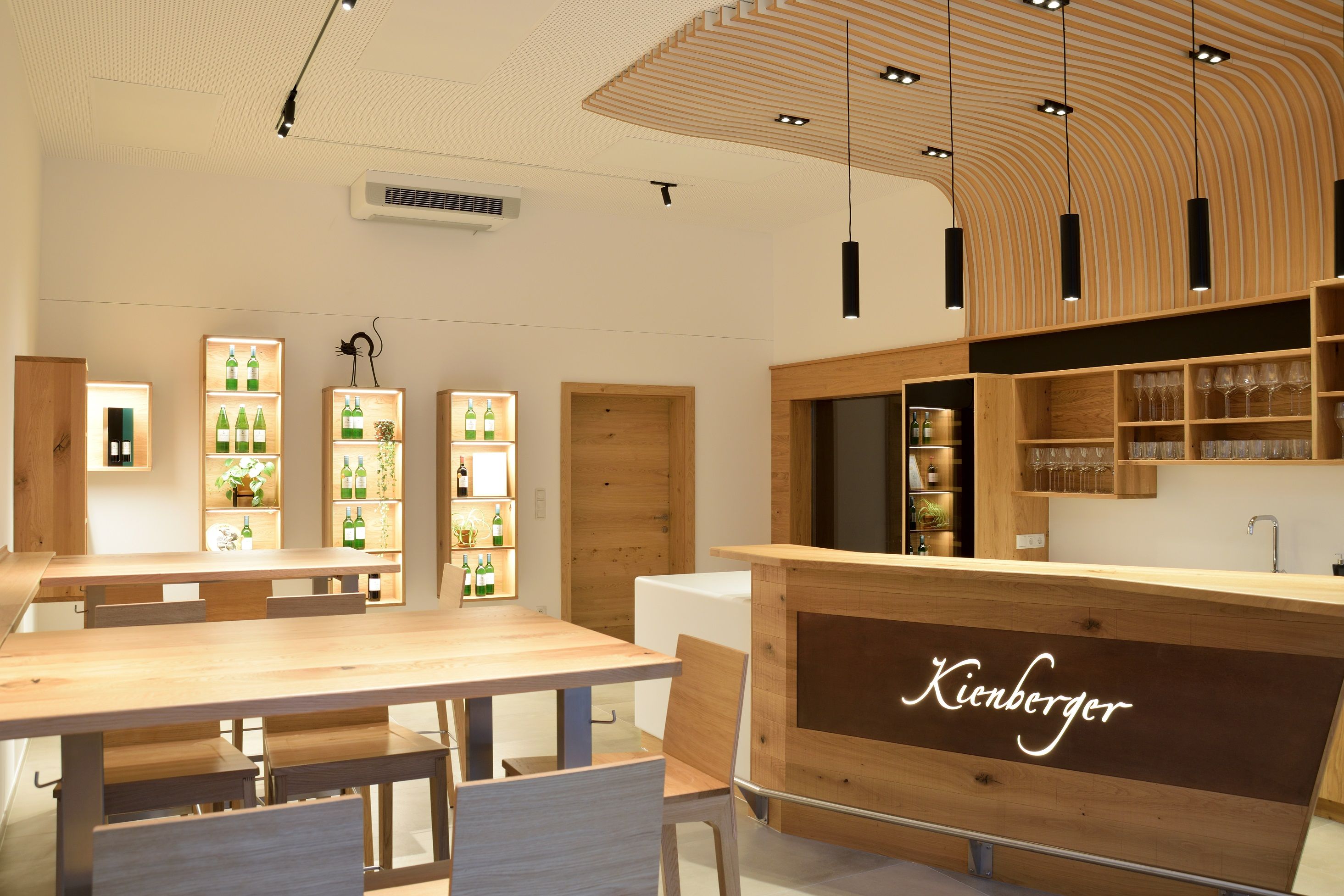 Moderner Verkostungsraum mit Holzmöbeln und beleuchteten Regalen mit Flaschen.