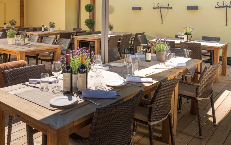 Eine Terrasse mit Holztischen, gedeckt mit Weinflaschen, Gläsern und Lavendel in Töpfen.