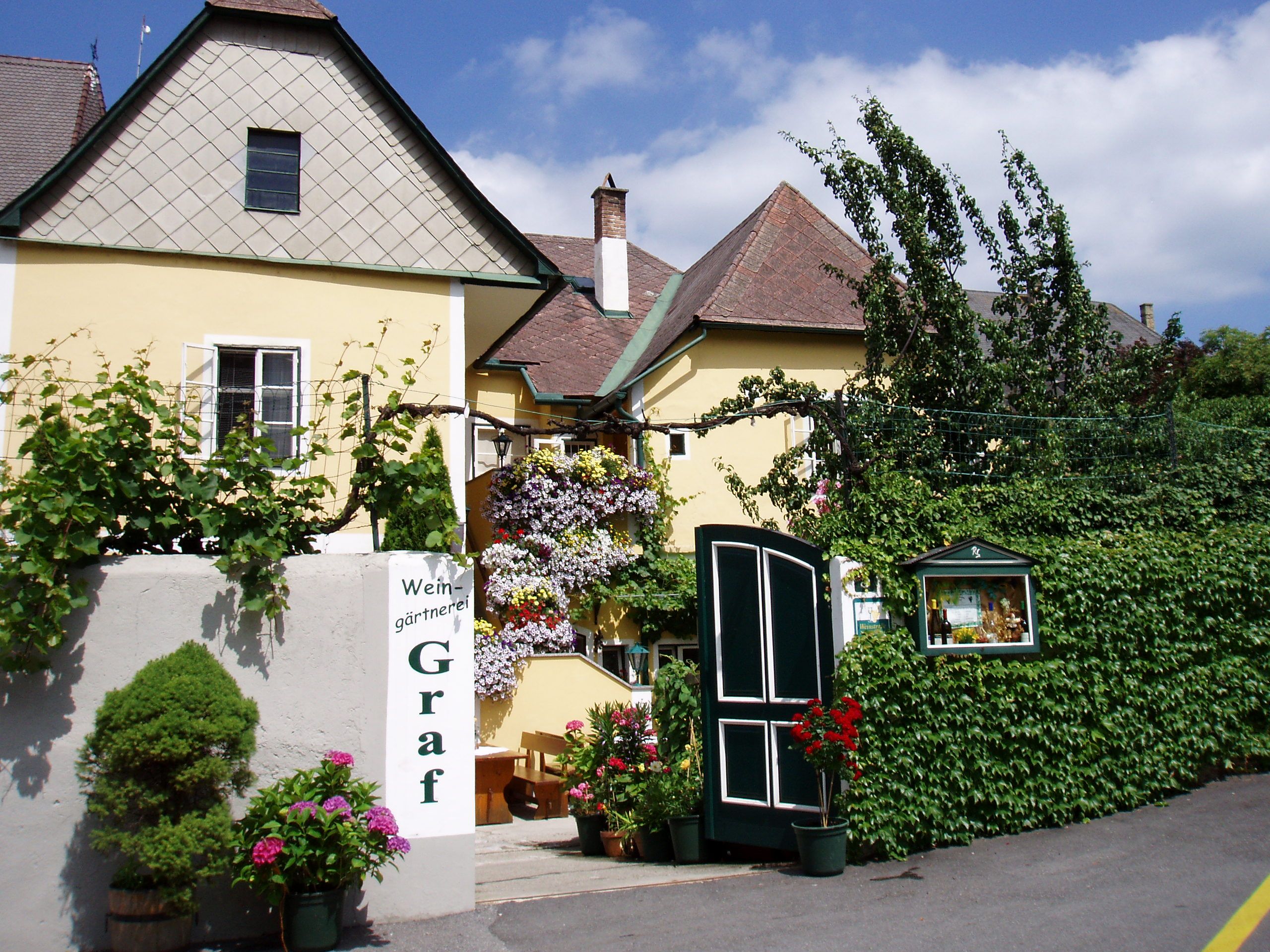 Außenansicht eines gelben Gebäudes mit Pflanzen und Blumen.