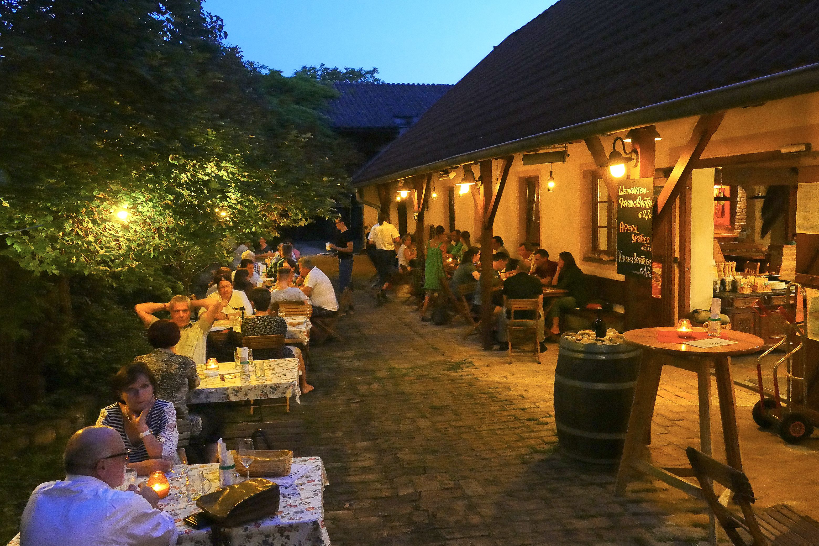Menschen sitzen abends in einem gemütlichen Außenbereich eines Buschenschanks.
