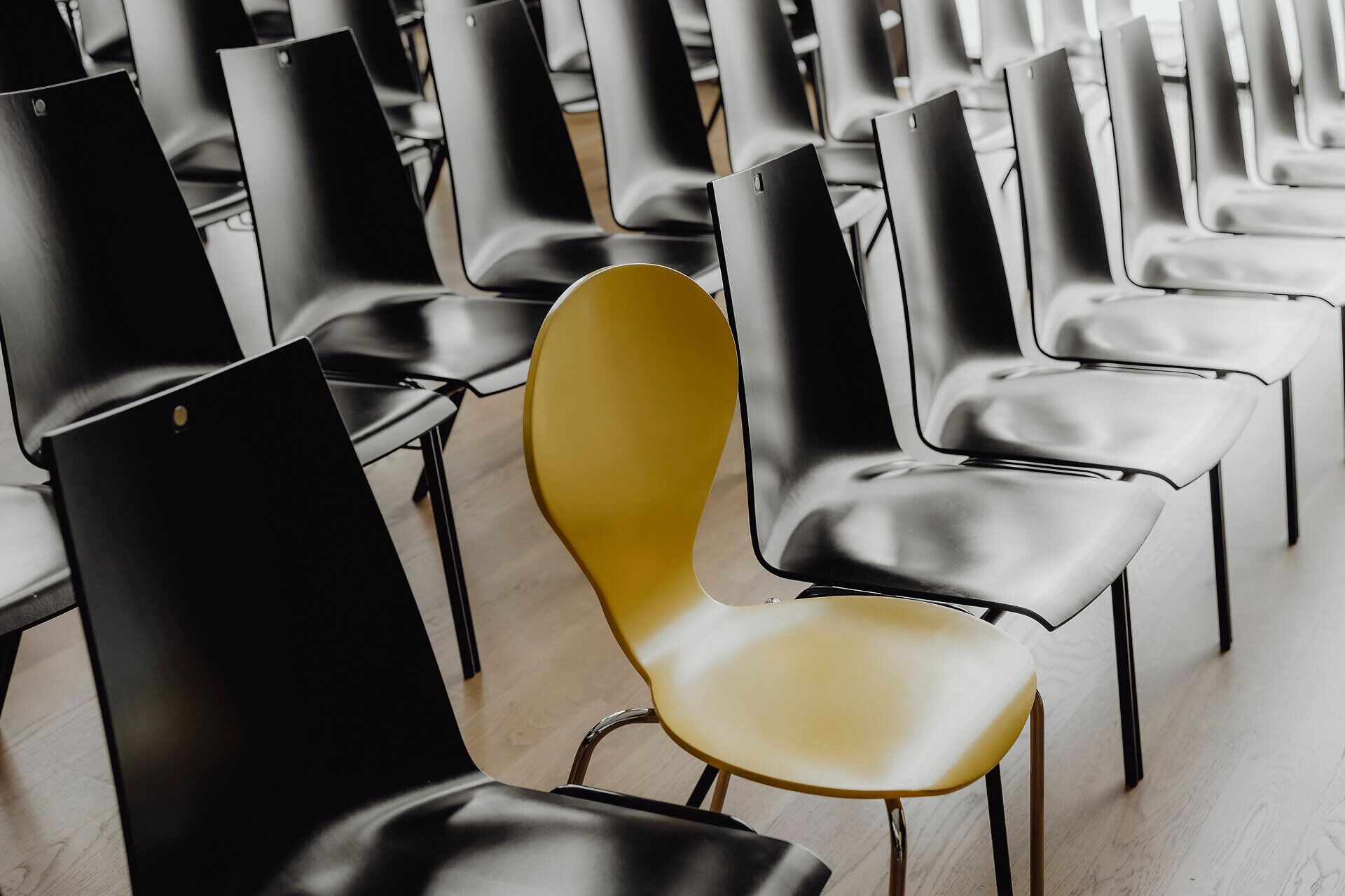 Die schlichten, eleganten Stühle in verschiedenen Farben schaffen eine einladende Atmosphäre für Veranstaltungen. Der gelbe Stuhl in der Mitte zieht die Blicke auf sich und lädt dazu ein, Platz zu nehmen und die Umgebung zu genießen. Hier wird Gemeinschaft und Austausch großgeschrieben.