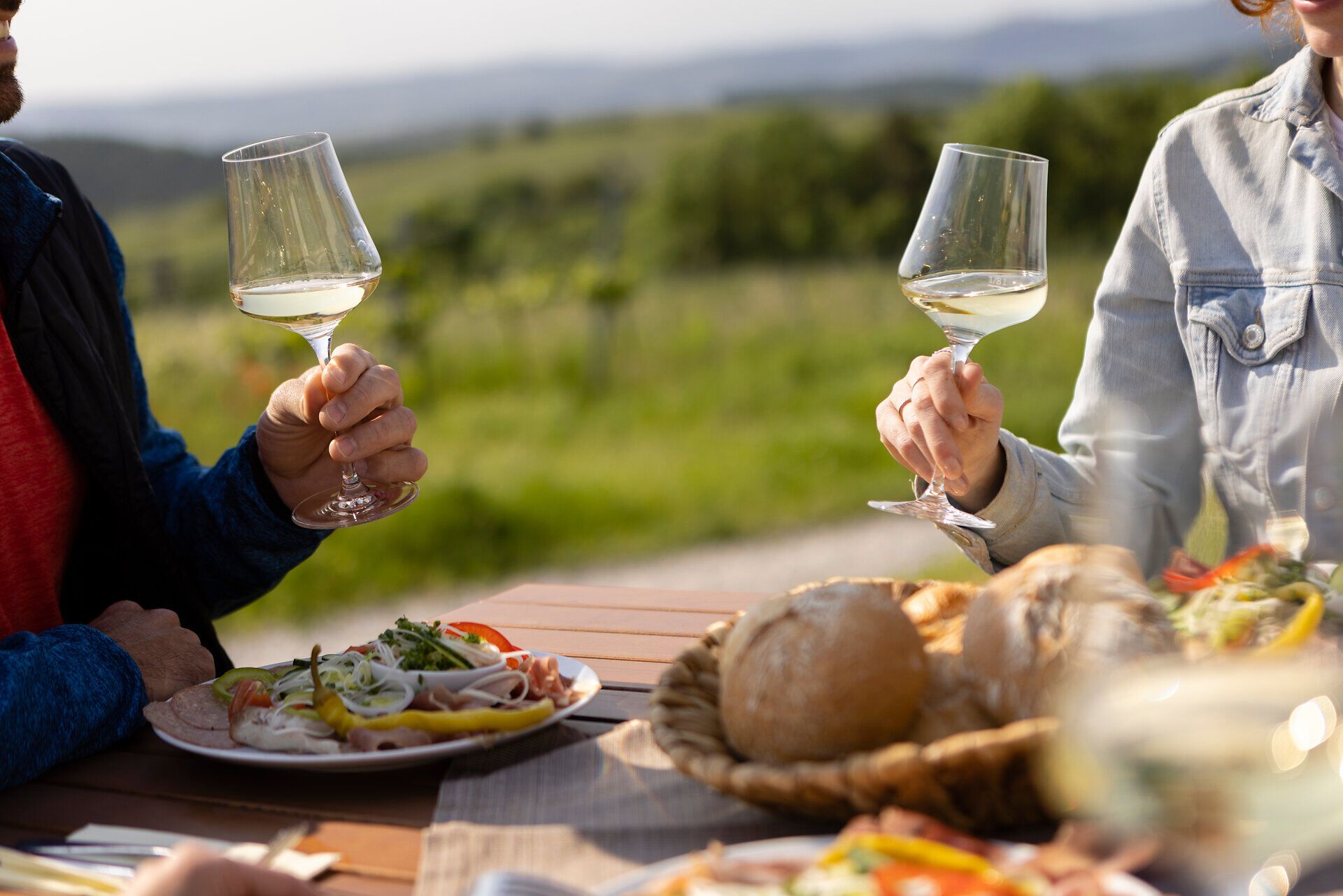Genießen Sie einen entspannten Moment inmitten der malerischen Landschaft, während Sie ein Glas erfrischenden Weißwein anstoßen. Die Tische sind liebevoll gedeckt mit köstlichen regionalen Spezialitäten, die den Gaumen verwöhnen. Umgeben von sanften Hügeln und üppigem Grün, lädt dieser Ort dazu ein, die Seele baumeln zu lassen und die Schönheit der Natur zu erleben.