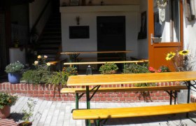 Ein gem&uuml;tlicher Au&szlig;enbereich eines Heurigen mit Holzb&auml;nken und Blumen.