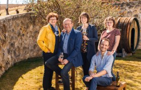 Eine Familie posiert l&auml;chelnd im Freien vor einer Steinmauer mit einem Weinfass im Hintergrund.