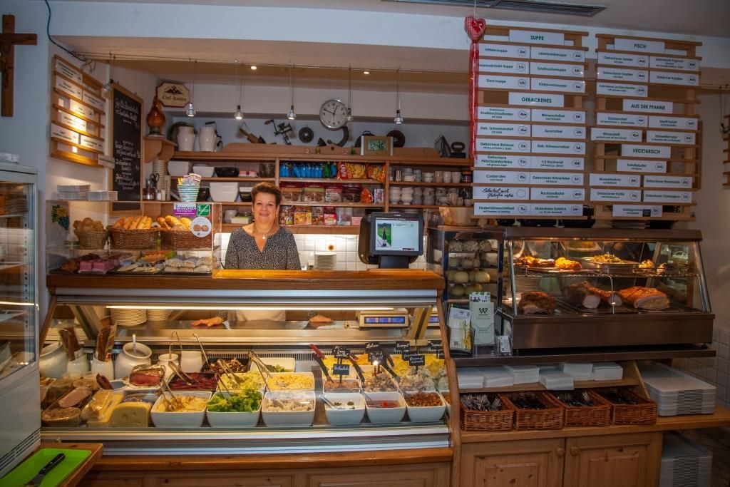 Frau hinter einem Buffet mit verschiedenen Speisen in einem Restaurant.