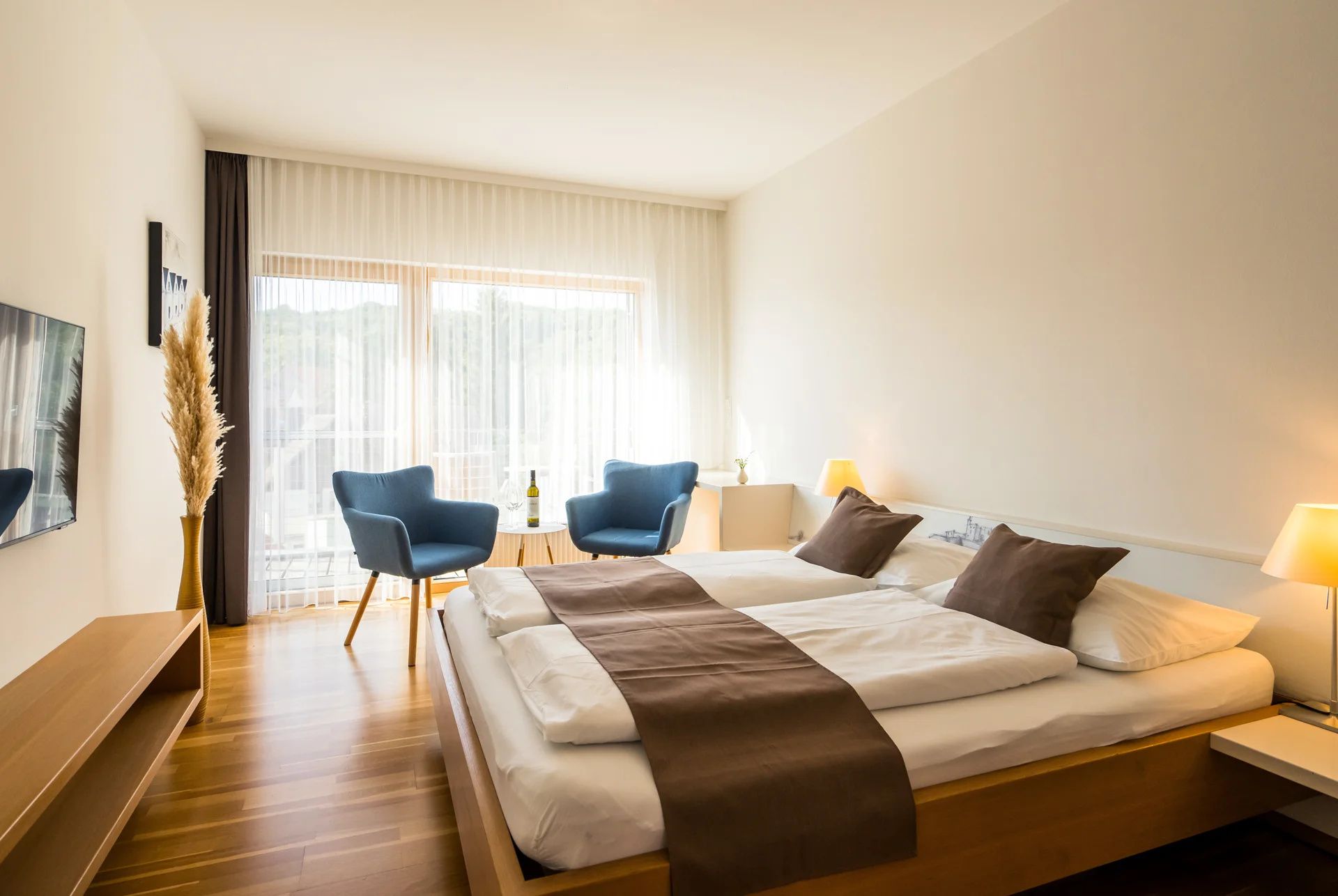 Modernes Gästezimmer mit Doppelbett, blauen Sesseln und Holzboden.