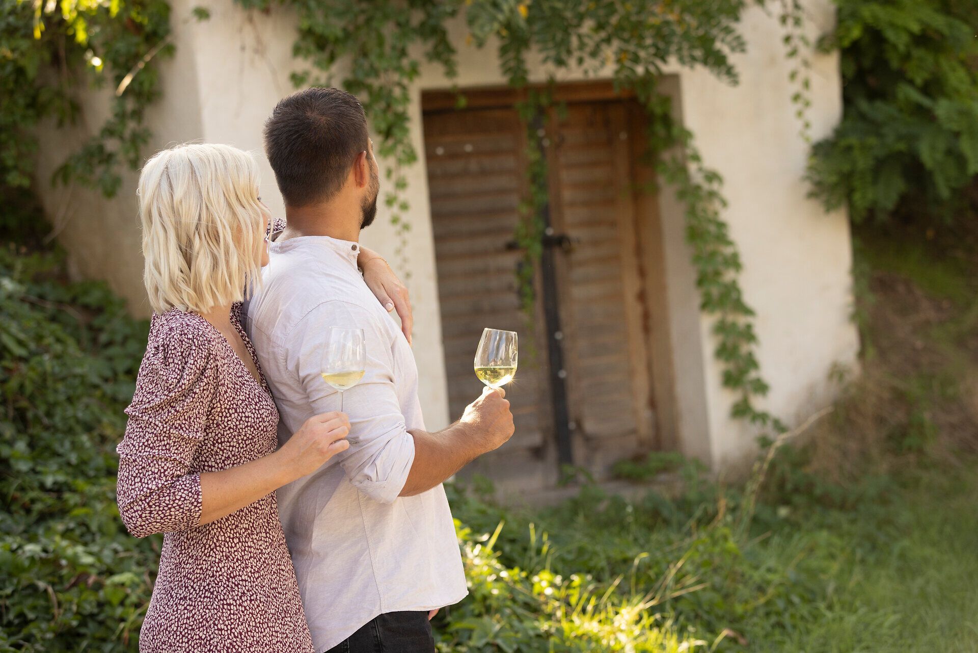 Ein Paar genießt einen entspannten Moment inmitten der Natur, während sie mit Gläsern in der Hand auf eine malerische Szenerie blicken. Die sanften Hügel und das üppige Grün schaffen eine romantische Atmosphäre, die zum Verweilen einlädt.