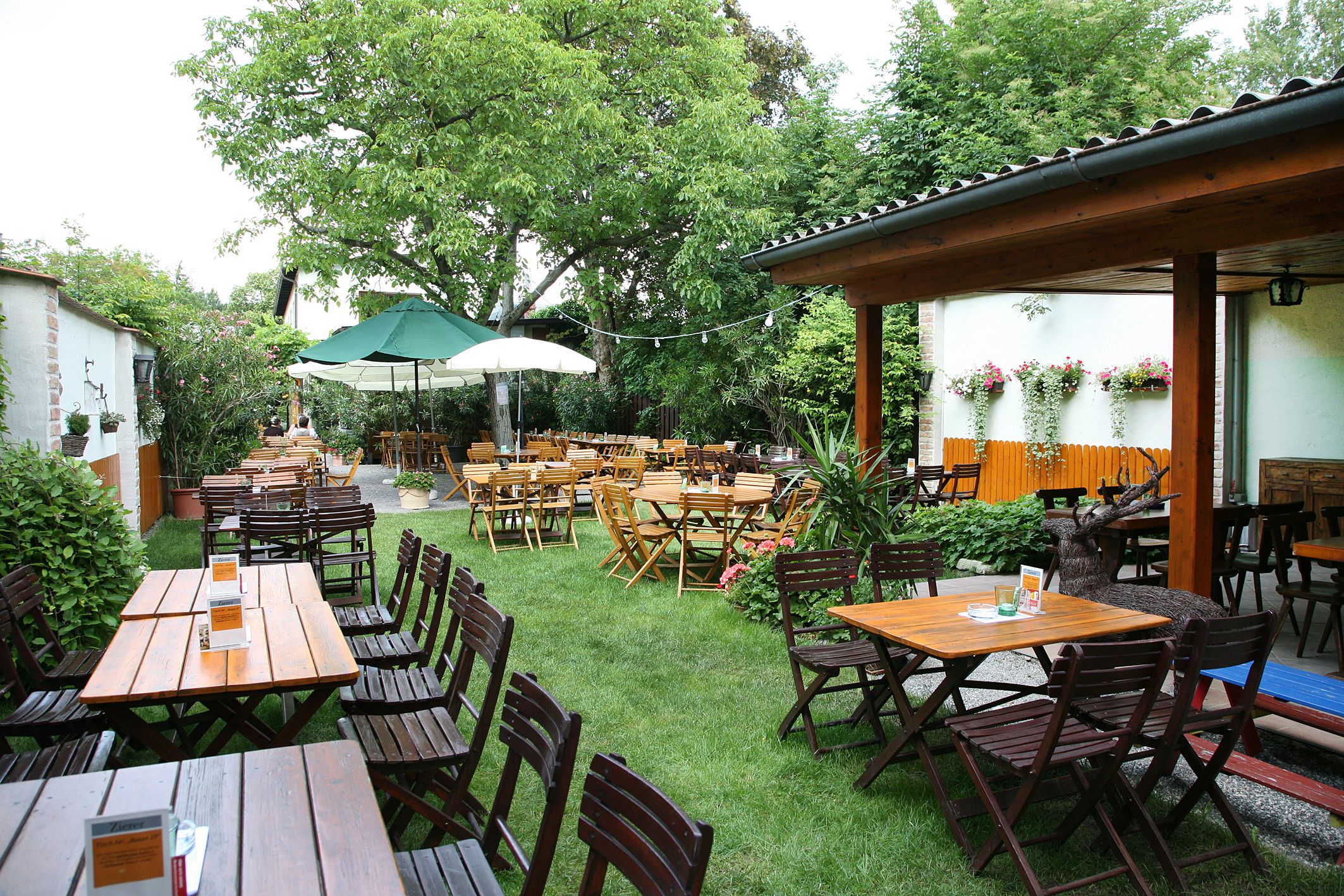 Ein gemütlicher Biergarten mit Holztischen und -stühlen, umgeben von grünen Bäumen und Pflanzen.