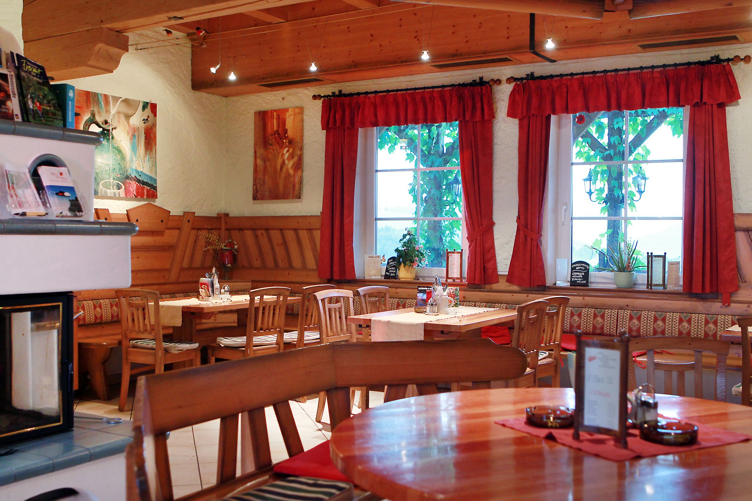 Gemütlicher Innenraum eines traditionellen österreichischen Heurigen mit Holzmöbeln und roten Vorhängen.