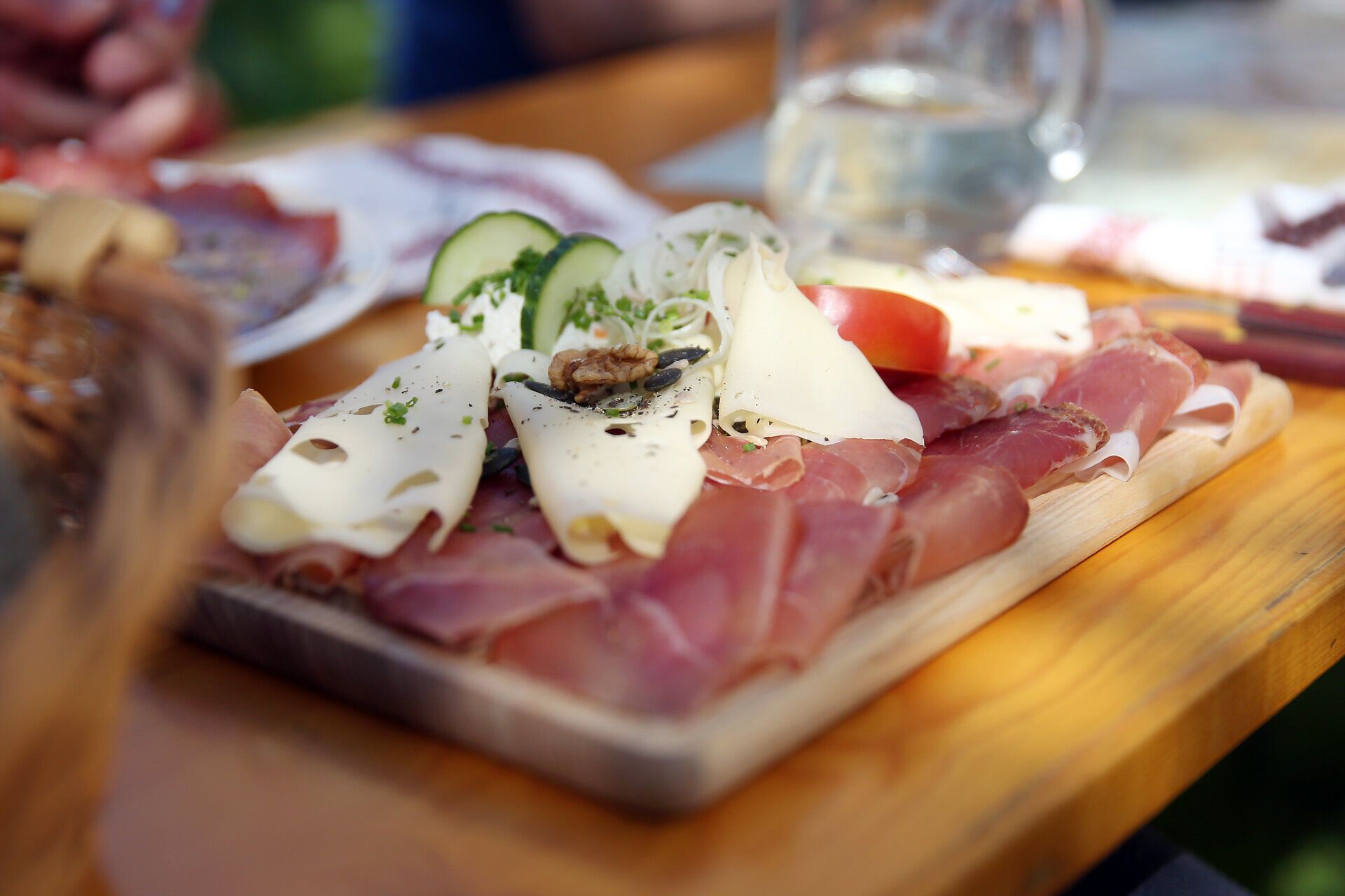 Genießen Sie die köstlichen Aromen der Heurigenjause, die auf einem rustikalen Holzbrett angerichtet ist. Zarte Schinken- und Käsesorten, begleitet von frischem Gemüse, laden zu einem geselligen Moment ein. Diese kulinarische Erfahrung verspricht, die Sinne zu verwöhnen und die Schönheit der Umgebung zu genießen.