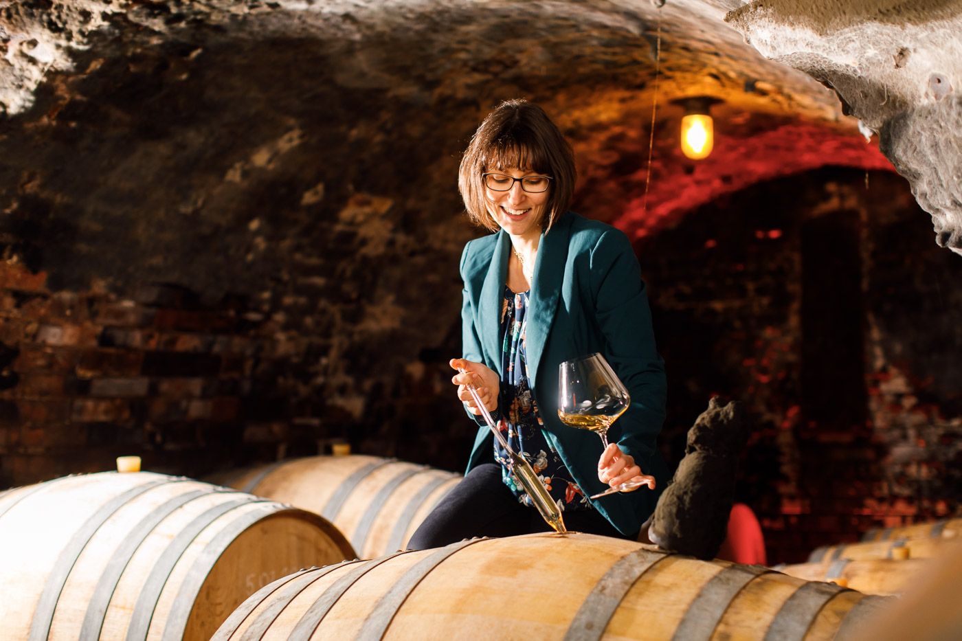 Frau bei Weinprobe im Weinkeller mit Weinglas und Fass.