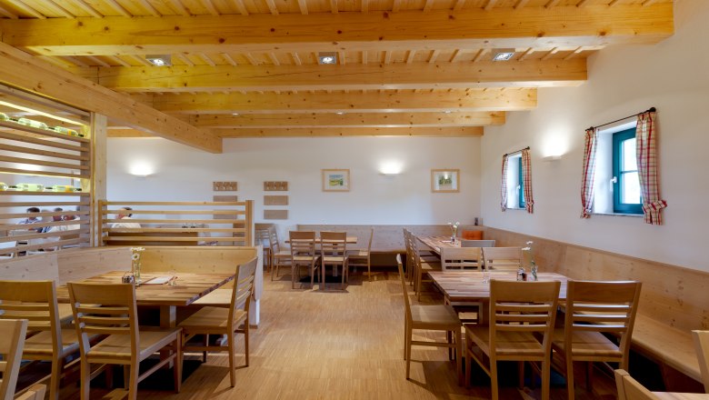 Innenansicht eines gem&uuml;tlichen Gastraums mit Holzm&ouml;beln und Holzbalkendecke.