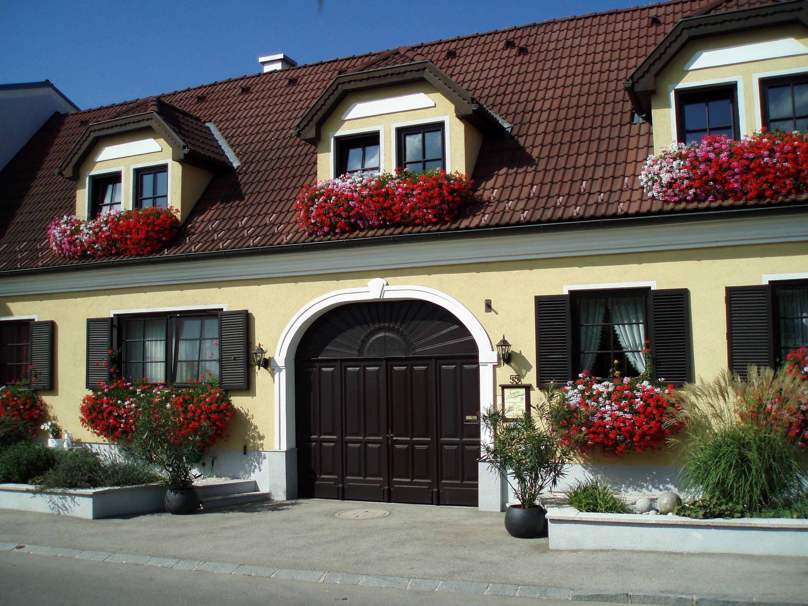 Gelbes Haus mit roten Blumen und braunem Dach.