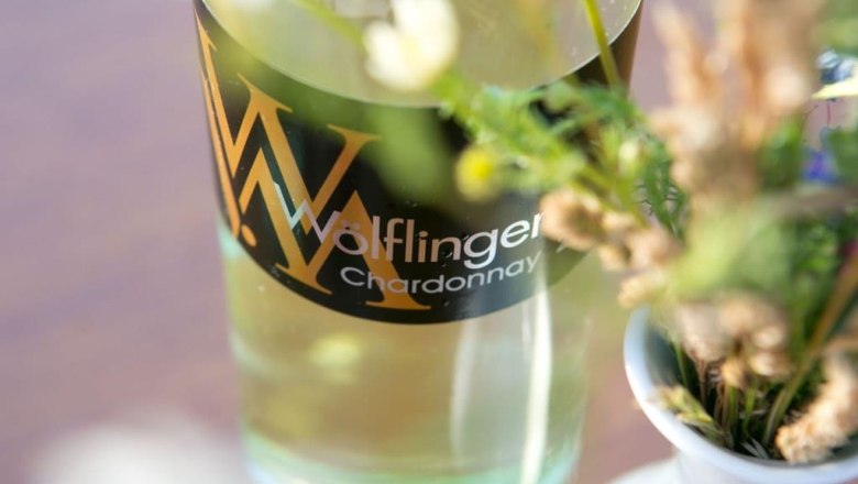 Nahaufnahme einer Weinflasche mit der Aufschrift 'Wölflinger Chardonnay' neben einem Blumenstrauß.
