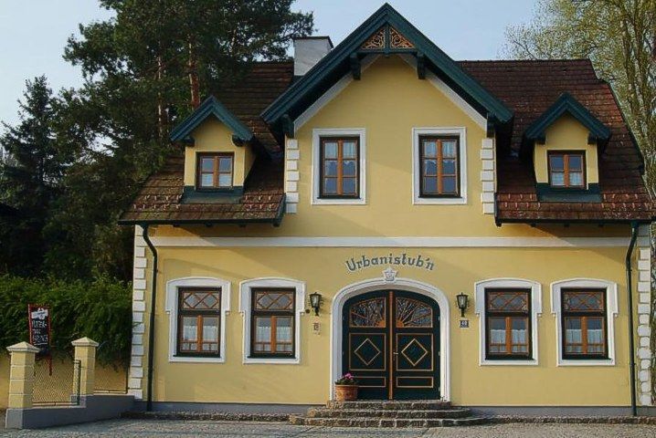 Gelbes Gebäude mit der Aufschrift 'Urbanistubn', umgeben von Bäumen.