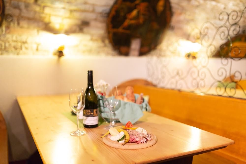 Ein Tisch in einem rustikalen Raum mit Weinflasche, Gläsern und einer Jause mit Brot und Aufschnitt.